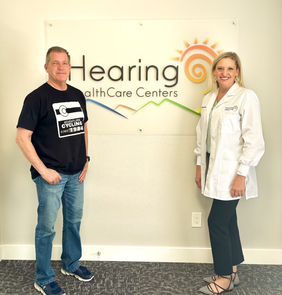 Jerry Schemmel and Dr. Whitney Swander in front of the Hearing HealthCare Centers logo