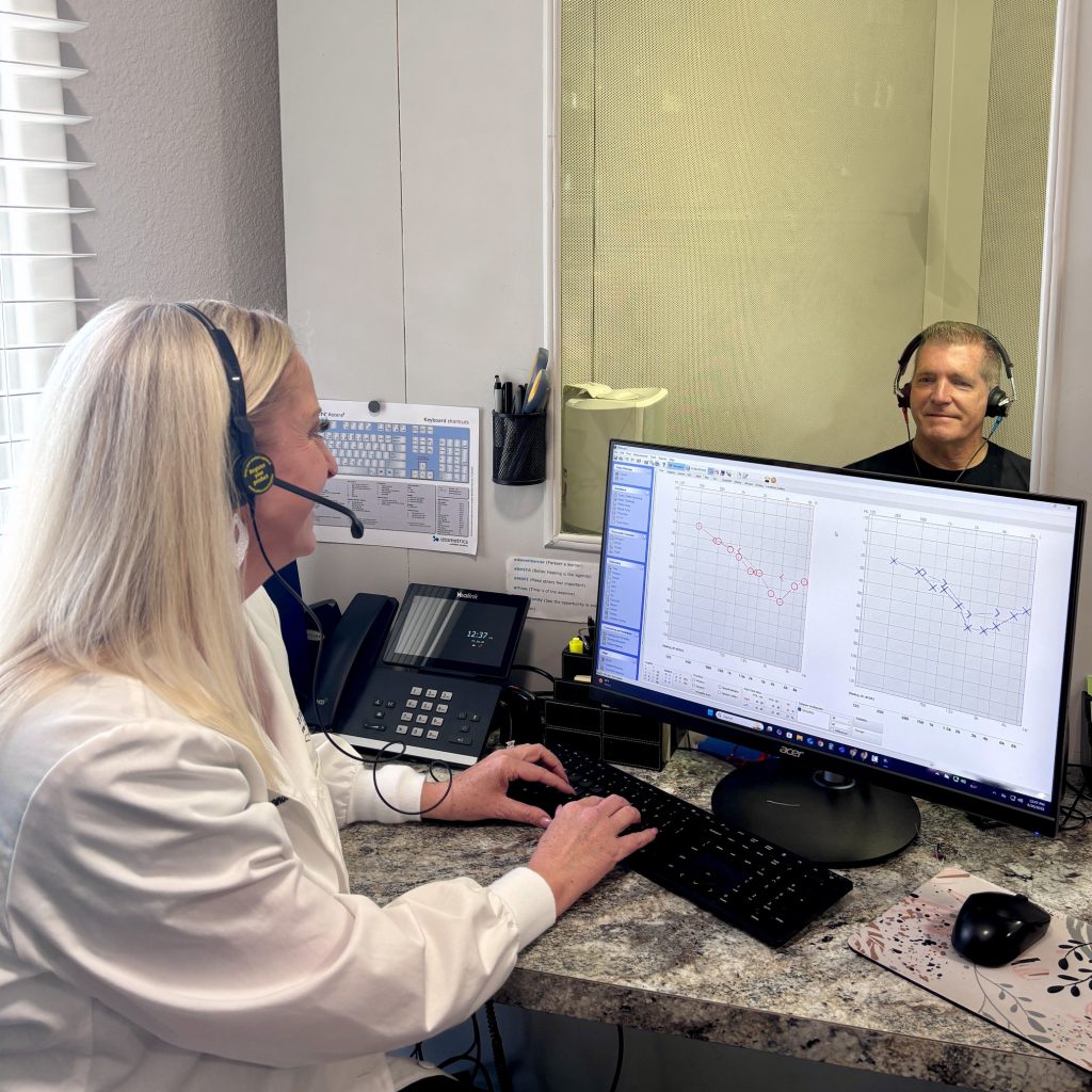 Jerry Schemmel in a hearing test booth with Dr. Whitney Swander