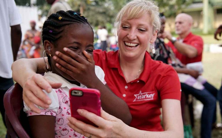 Dr. Swander looking at a phone with a young girl with hearing aids in the Congo